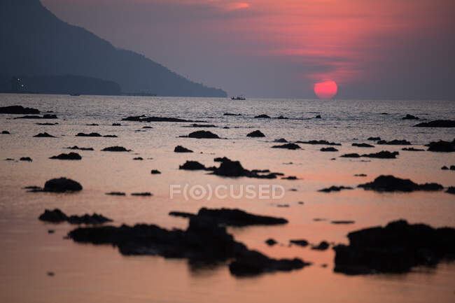 Широке узбережжя з морськими водоростями, що розбризкують море проти пагорба і червоне сонце в Малайзії. — стокове фото