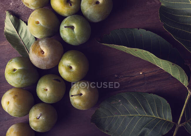 From above of fresh ripe plums and green leaves placed on wooden table in daytime — Stock Photo