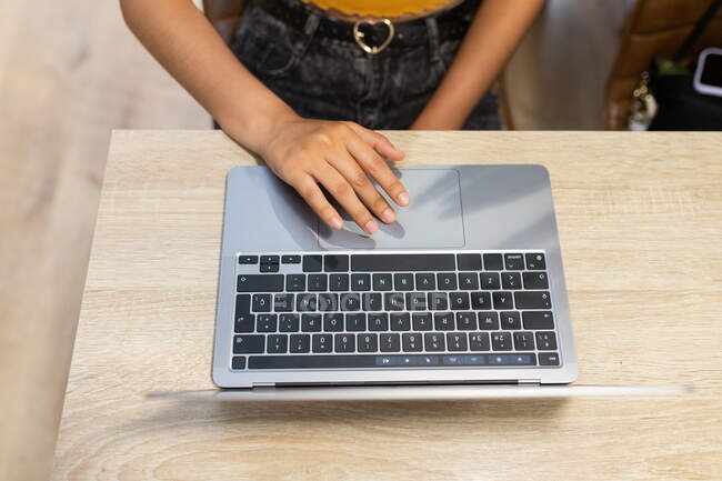 From above cropped unrecognizable young female entrepreneur sitting at table and browsing netbook while working on modern workplace — Stock Photo