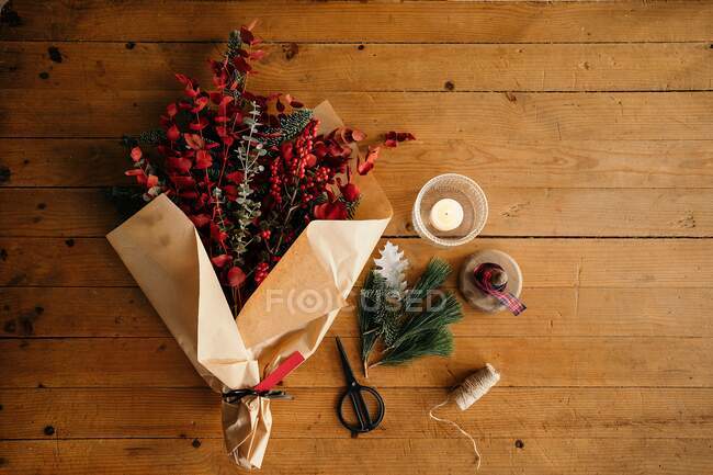 From above of Christmas bouquet in wrapping paper placed near scissors and decorative equipment on wooden table in daylight — Stock Photo