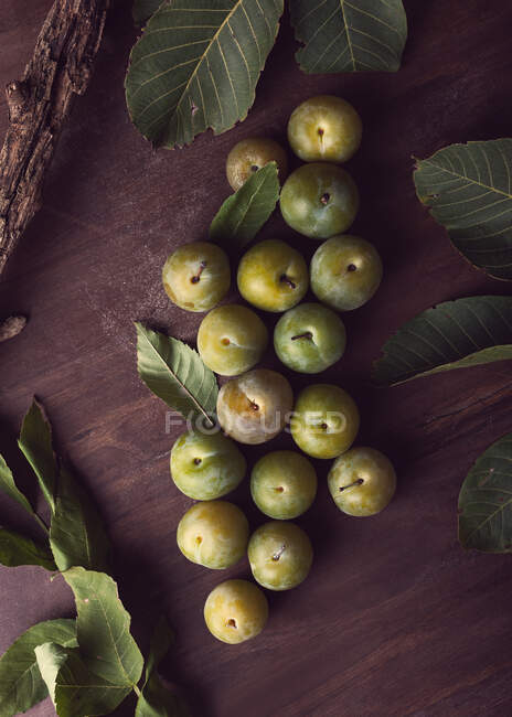 De dessus de prunes fraîches mûres et de feuilles vertes placées sur une table en bois le jour — Photo de stock