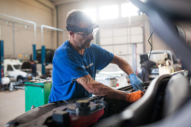 Side view of busy mature male technician fixing engine of broken car in spacious facility of repair service — Stock Photo