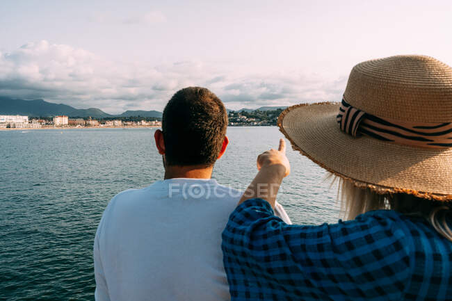 Повернення до анонімної пари туристів, які споглядають море і піднімаються під хмарним блакитним небом у Сен-Жан-де-Луз. — стокове фото