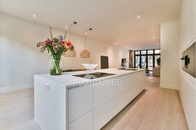 Interior de cozinha contemporânea com fogão elétrico contra vaso com flores em flor e construído em forno em casa — Fotografia de Stock