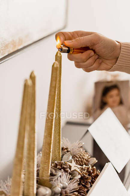 Cultive a pessoa irreconhecível que ilumina a vela decorativa entre cones coníferas enquanto celebra férias de Ano Novo na casa — Fotografia de Stock
