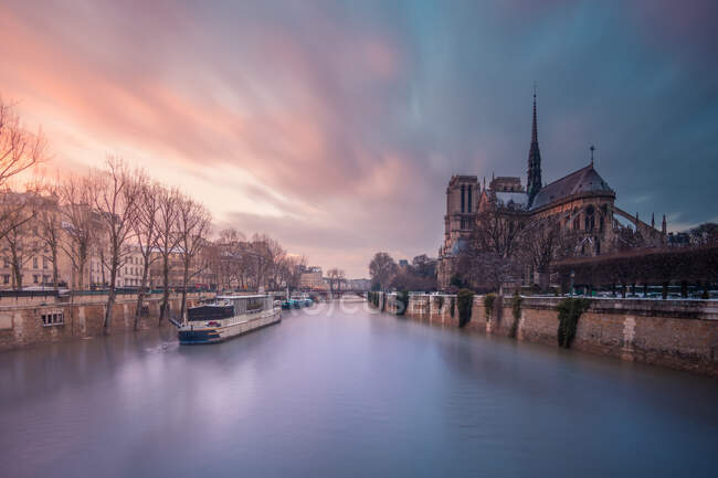 Navio turístico flutuando em águas ondulantes do rio Sena passando pela catedral católica medieval Notre Dame de Paris ao pôr-do-sol — Fotografia de Stock