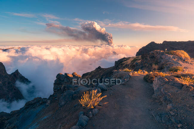 Salida del sol en un sendero de montaña de gran altitud en medio de nubes blancas suaves y gruesas y la erupción de un volcán en el fondo. Cumbre Vieja erupción volcánica en La Palma Islas Canarias, España, 2021 - foto de stock