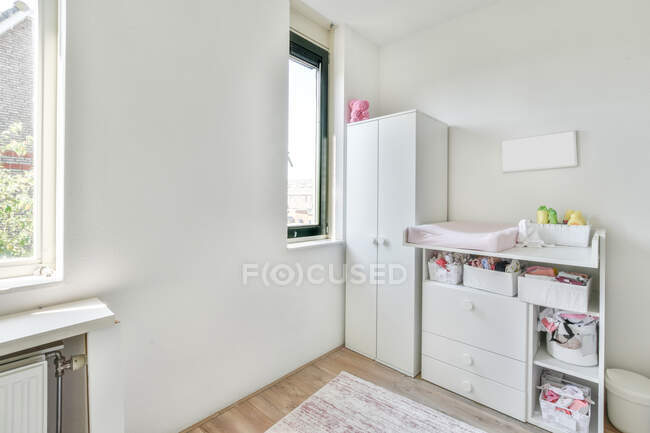 Minimalistisches Interieur eines hellen Zimmers mit weißem Kleiderschrank und Schrank mit Regalen, die tagsüber neben dem Fenster stehen — Stockfoto