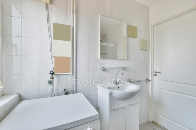 Интерьер просторной ванной комнаты с белой плиткой стен и зеркало над керамической раковиной разработан в минимальном стиле — стоковое фото