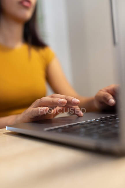 Cropped unrecognizable young female entrepreneur sitting at table and browsing netbook while working on modern workplace — Stock Photo