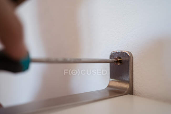 Cropped unrecognizable male with manual screwdriver screwing shelf to wall in house room — Stock Photo