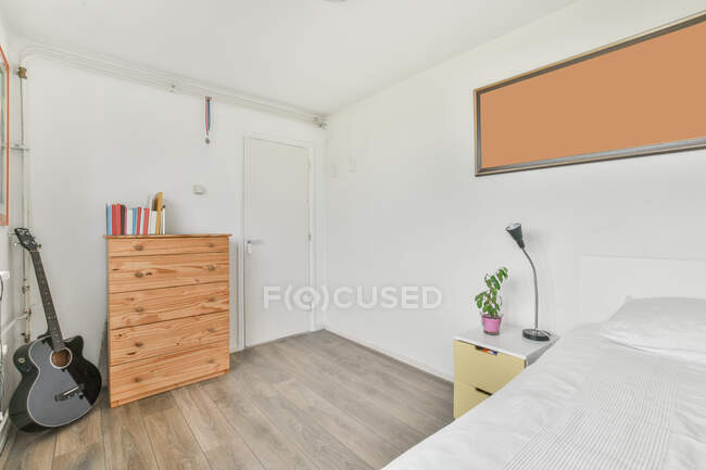 Интерьер современной светлой спальни с удобной кроватью возле стены с гитарой — стоковое фото