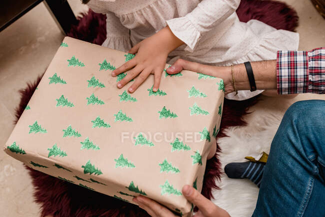 Cropped unrecognizable child opening present box between anonymous father during New Year holiday at home — Stock Photo