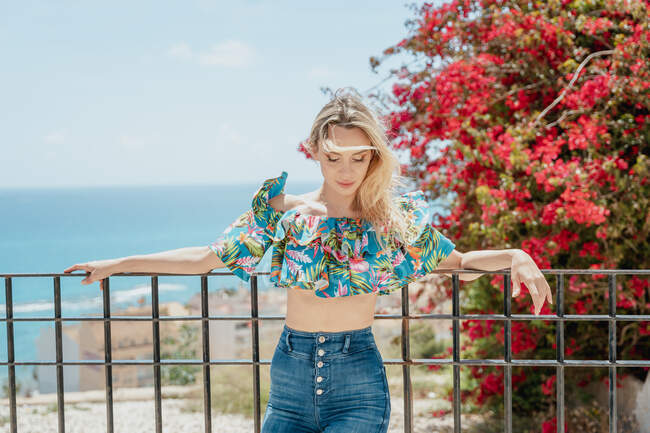 Confident female in top and jeans on terrace of building on shore of sea and looking away — Stock Photo