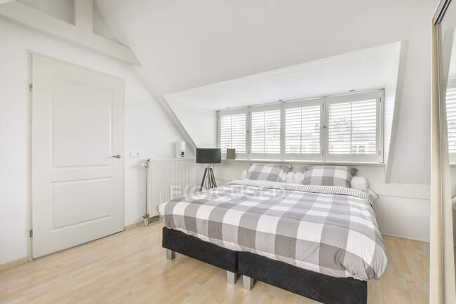 Комфортне м'яке ліжко з білим ковдрою, розміщене біля великих вікон в сучасній спальні в квартирі — стокове фото