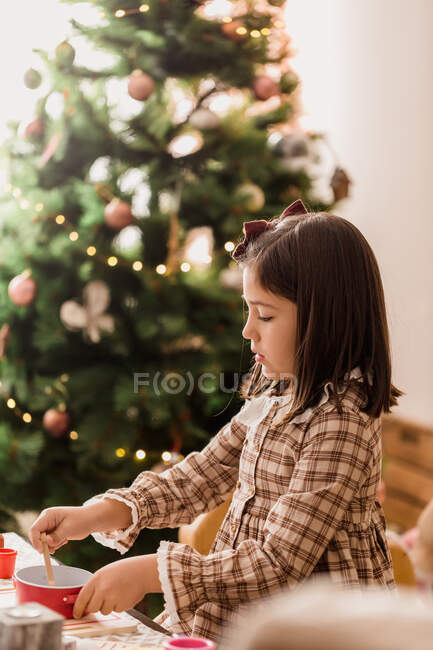 Aufmerksames Kind in kariertem Kleid spielt beim Kochen am Tisch im hellen Raum mit Spielzeug — Stockfoto