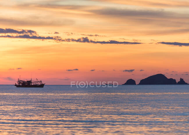 Silhouette of fishing boat swimming on endless sea under colorful orange sundown sky in Malaysia — Stock Photo