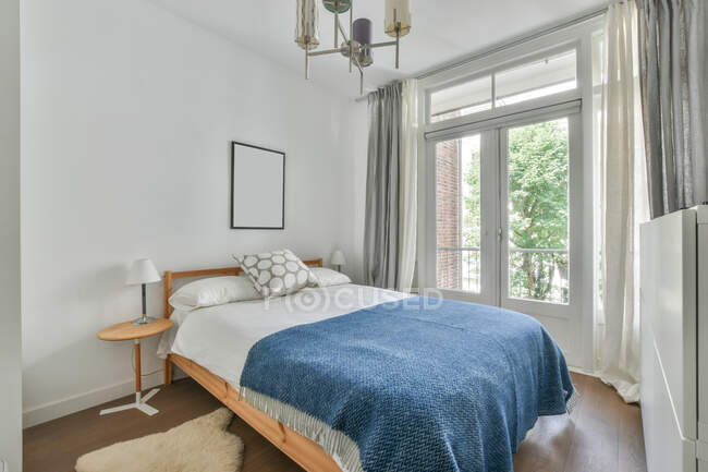 Interno di elegante camera da letto con comodo letto vicino alla finestra e pareti luminose durante il giorno — Foto stock