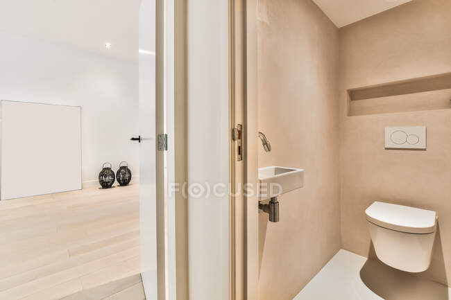 Креативный дизайн ванной комнаты с настенным туалетом против умывальника и декоративными вазами на паркете в светлой комнате дома — стоковое фото