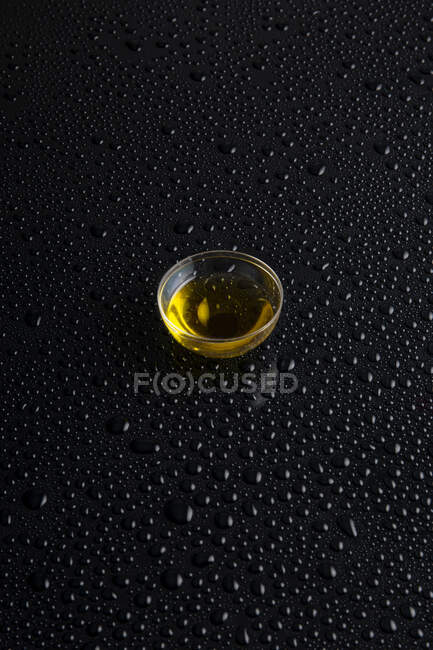 From above of transparent glass bowl with oil on black background covered with clear drips — Stock Photo
