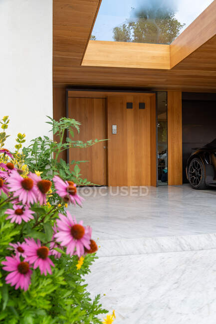 Villa de lujo patio con flores florecientes y coche moderno estacionado en garaje con paredes de madera y ascensor - foto de stock