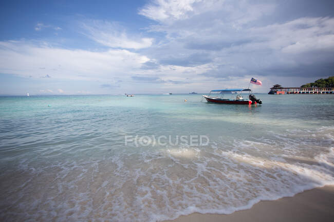 Човен з національним прапором на ясному блакитному морі, який котиться на мокрому піщаному пляжі в Малайзії. — стокове фото