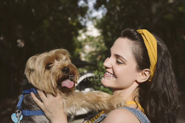 Side view of happy female owner smiling widely while enjoying time with funny Yorkshire Terrier with tongue out — Stock Photo