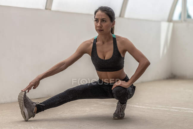 Young flexible ethnic sportswoman in active wear stretching leg during workout in daytime — Stock Photo