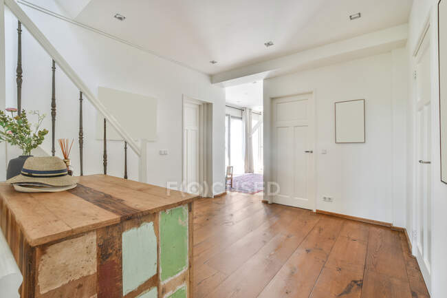 Sombreros de paja en mesa de madera envejecida en el suelo contra puertas y barandilla de escalera en el pasillo en casa - foto de stock