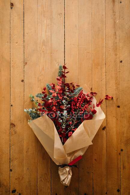 Von oben ein festlich-stilvoller dekorativer Weihnachtsstrauß mit Eukalyptuszweigen und leuchtend roten Zweigen mit Beeren auf dem Holztisch im Zimmer — Stockfoto