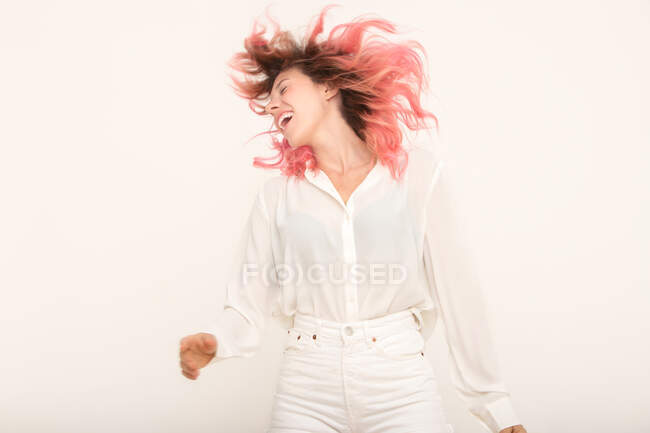 Sorridente giovane femmina in abiti eleganti in piedi e scuotendo i capelli rosa sullo sfondo chiaro in camera — Foto stock