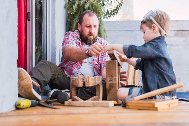 Первый уровень веселого бородатого папы в клетчатой рубашке с мальчиком, работающим с деревянными блоками — стоковое фото
