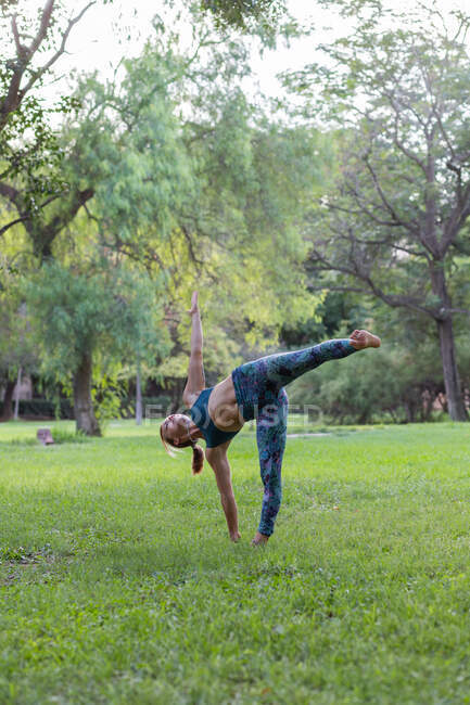 Full body of flexible female in activewear doing Ardha Chandrasana during yoga practice in green park in daytime — Stock Photo