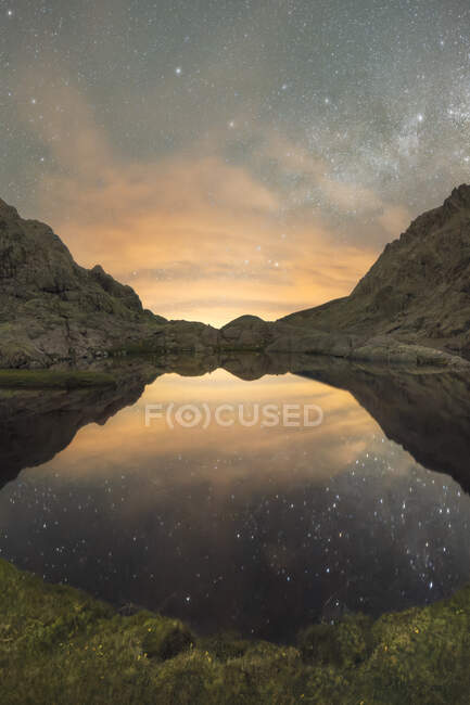 Espectacular paisaje de río tranquilo que refleja ásperas montañas rocosas bajo cielo estrellado sin nubes en el crepúsculo - foto de stock
