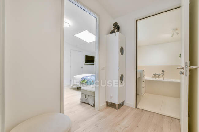 Letto sotto lampada lucida contro bagno contemporaneo con vasca e mobile su pavimento piastrellato a casa — Foto stock