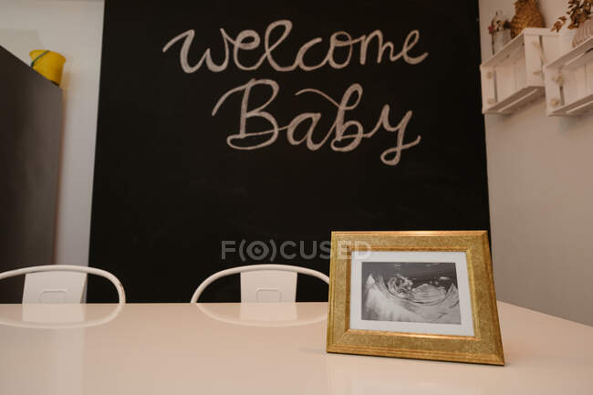 Ultraschallbild von Baby auf Tisch gegen Willkommensbaby-Inschrift auf Kreidetafel im Esszimmer — Stockfoto