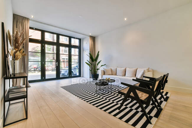 Интерьер современной комнаты с диваном и креслами на ковре с полосатым орнаментом на паркете в доме — стоковое фото