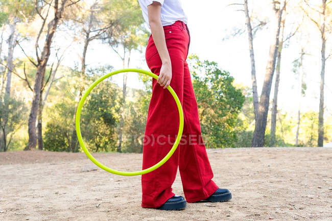 Vista laterale del raccolto adolescente donna irriconoscibile in jeans rossi con hula hoop pur avendo tempo libero nel parco — Foto stock