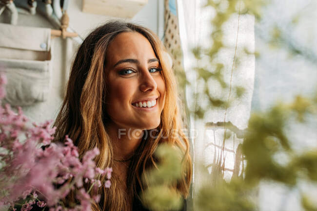 Portrait of gorgeous teen girl at home behind colorful flowers and looking at camera — Stock Photo