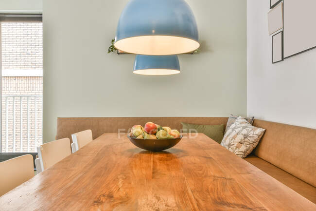 Interior do moderno apartamento espaçoso mobilado com sofá de canto perto de mesa de madeira e cadeiras sob lâmpadas penduradas no teto — Fotografia de Stock