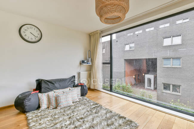 Interior de quarto contemporâneo com almofadas e pufes em tapete fofo em parquet contra parede de janela em casa — Fotografia de Stock