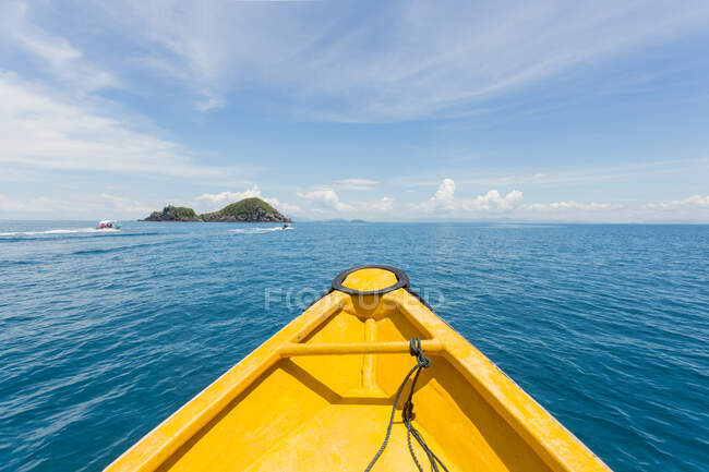 Яркая плывущая лодка, плывущая по синему волнообразному морю к холмам в солнечный день в Малайзии — стоковое фото