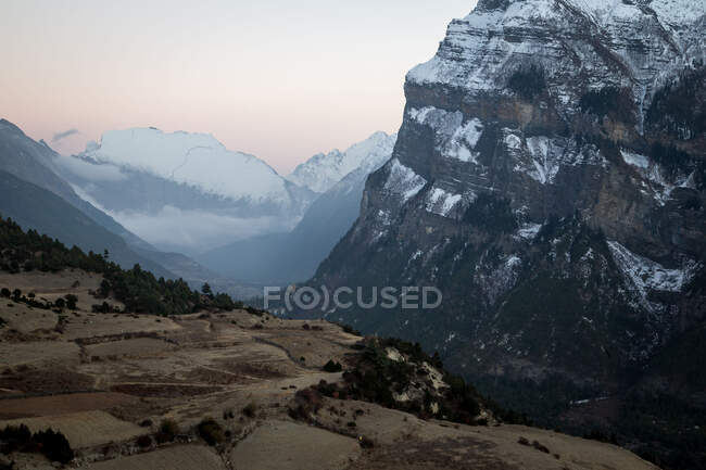 Altas laderas empinadas de montañas cubiertas de nieve ubicadas en el valle del Himalaya se extienden bajo un cielo colorido en Nepal - foto de stock