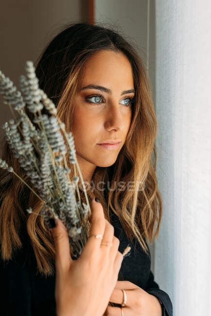 Portrait of gorgeous teen girl at home holding a branch of lavender and looking away — Stock Photo