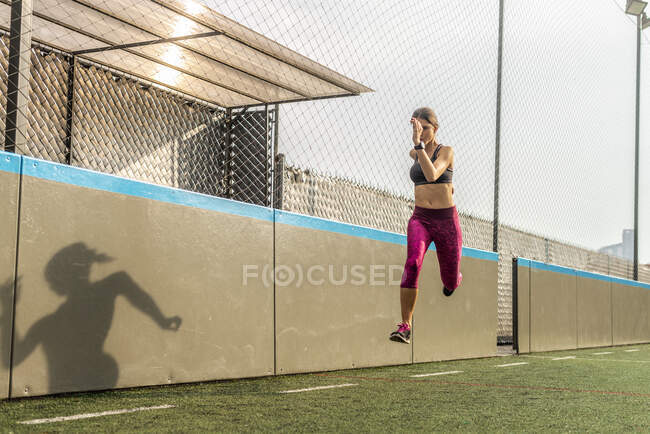 Corps entier d'athlète féminine durable en vêtements de sport sautant au-dessus du sol pendant l'entraînement intense dans le stade — Photo de stock