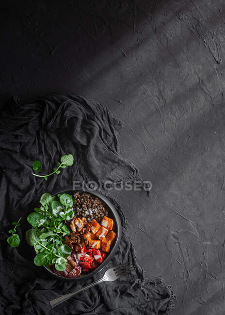 Вид зверху салат з гарбузом і болгарським перцем, прикрашений зеленим листям базиліка на чорному тлі — стокове фото