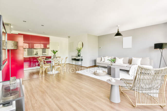 Интерьер гостиной с удобным диваном и креслом и кухней с красной мебелью в современной квартире открытой планировки — стоковое фото