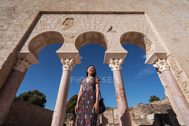 Dal basso asiatico viaggiatore femminile in piedi vicino alla pietra antico portico con colonne e passaggi ad arco durante il viaggio nella città di Cordova — Foto stock