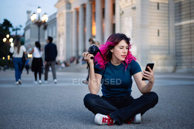 Ganzkörper-Fotografin mit rosa Haaren und Fotokamera in der Hand surft auf dem Gehweg in der Nähe eines alten Gebäudes in der Stadt — Stockfoto