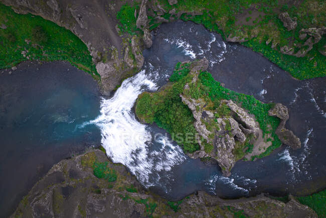 Drone vista de río rápido que fluye entre ásperas costas rocosas empinadas cubiertas de musgo verde en la naturaleza salvaje de Islandia - foto de stock